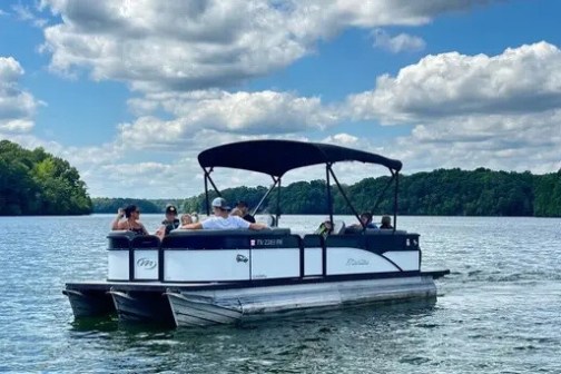 Group on pontoon boat in a lake under cloudy sky.