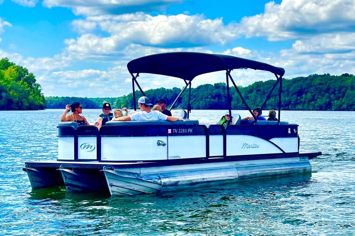 People relaxing on a pontoon boat in a lake surrounded by trees.
