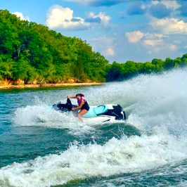 Person riding a jet ski on a lake with trees in the background.