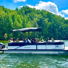 Group of people on a pontoon boat in a lake with forested shore.