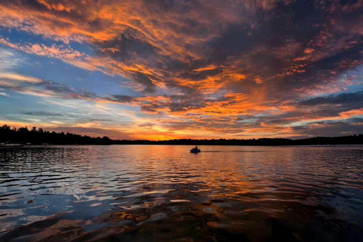 A vibrant sunset over a calm lake with a silhouetted boat in the distance.