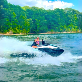 Person riding a jet ski on a lake with forested shoreline.