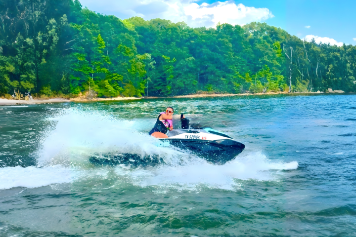 Person riding a jet ski on a lake with forested shoreline.