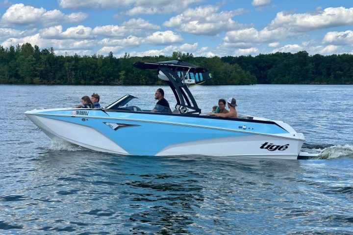White and blue motorboat with people on a lake under partly cloudy skies.