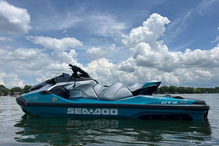 Blue and gray jet ski floating on a calm lake under a cloudy sky.